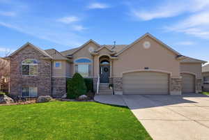 View of front facade featuring an attached garage, stucco siding, driveway, a front yard, and brick siding