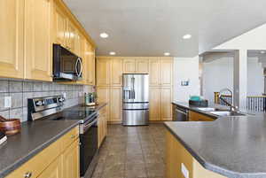 Kitchen with stainless steel appliances, light wood finish cabinets, dark countertops, and recessed lighting