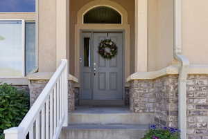 Doorway to property featuring stone siding, stucco siding, and a porch