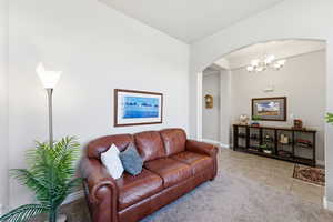Living area with light colored carpet, arched walkways, suspended lighting, and light tile patterned floors