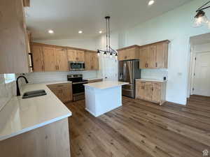 Kitchen featuring backsplash, stainless steel appliances, vaulted ceiling, decorative light fixtures, and dark wood-type flooring