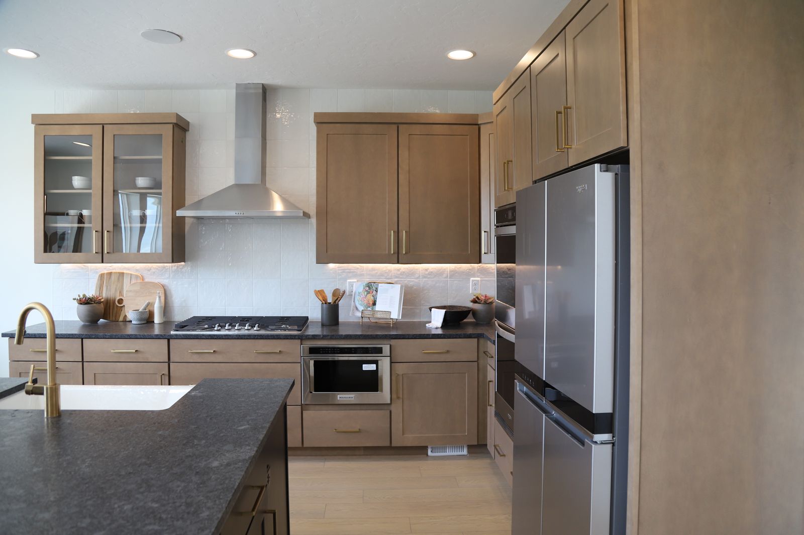 Kitchen with dark stone counters, glass insert cabinets, stainless steel appliances, backsplash, and light wood-style floors
