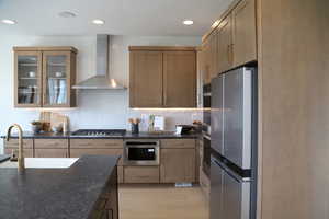Kitchen with dark stone counters, glass insert cabinets, stainless steel appliances, backsplash, and light wood-style floors