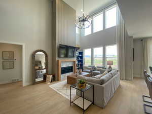 Living room featuring a high ceiling, a tile fireplace, light wood-style floors, suspended lighting, and healthy amount of natural light