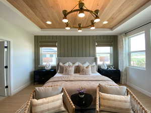 Bedroom with a wood tray ceiling, light wood-type flooring, and suspended lighting