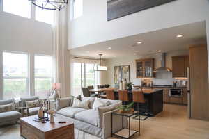Living area featuring light wood-type flooring, suspended lighting, and a high ceiling