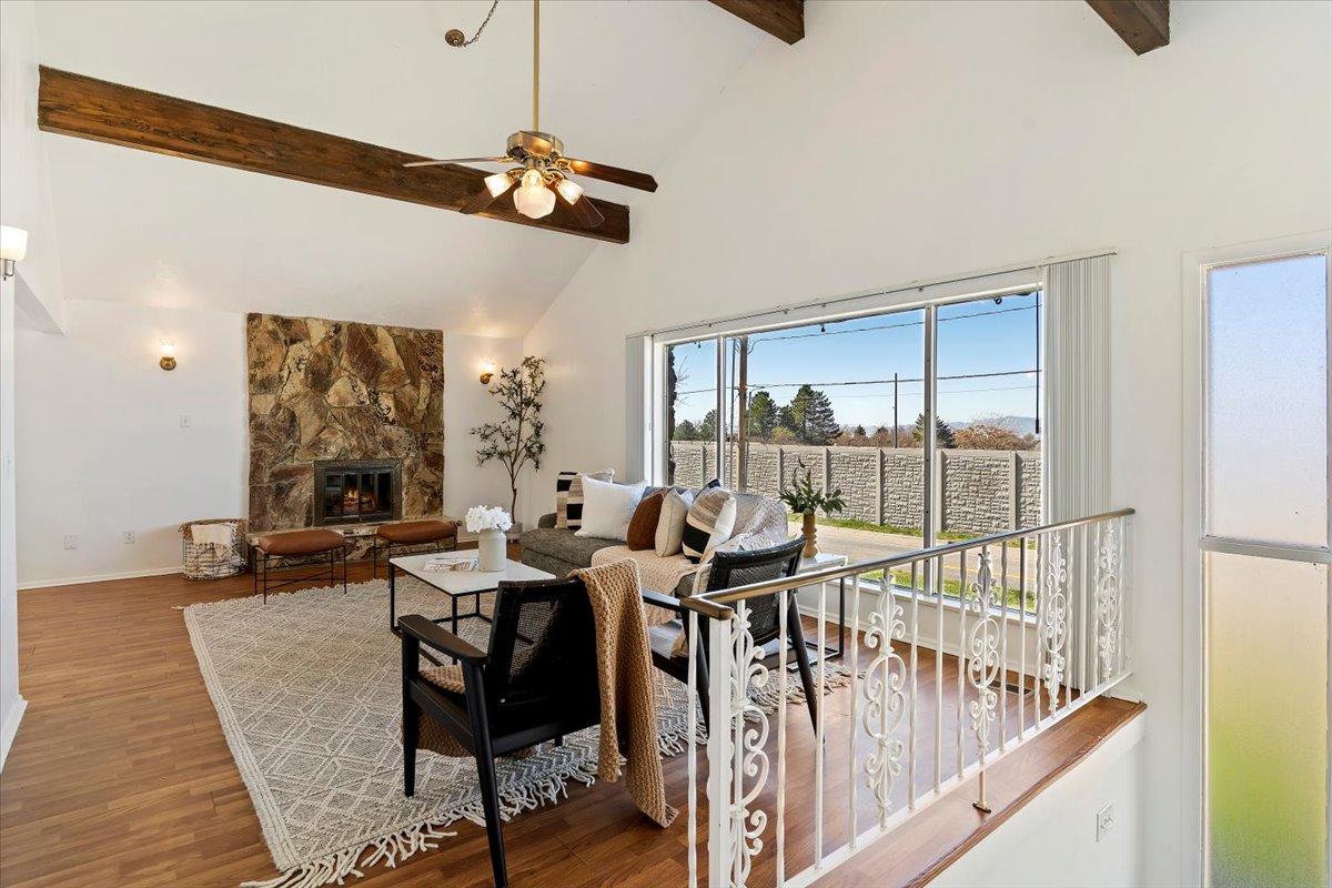 Living area with a stone fireplace, lofted ceiling, wood finished floors, and ceiling fan