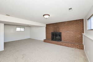 Unfurnished living room featuring a fireplace, carpet, a textured ceiling, and brick wall