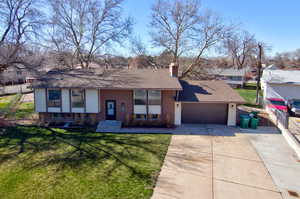 View of front of house featuring driveway, a chimney, an attached garage, roof with shingles, and brick siding