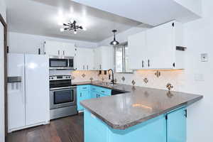 Kitchen with dark countertops, stainless steel appliances, a peninsula, hanging light fixtures, and two tone cabinets