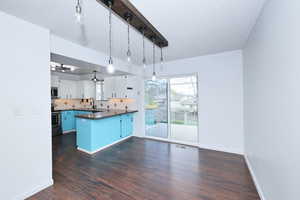 Kitchen featuring a peninsula, a textured ceiling, decorative backsplash, dark wood-type flooring, and stainless steel appliances