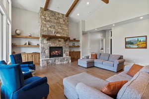 Living room featuring light wood floors, a stone fireplace, and vaulted ceiling with custom beams.