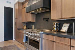 Kitchen featuring dark countertops, range with two ovens, tasteful backsplash, and light wood-style floors