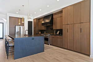 Kitchen featuring modern cabinets, premium appliances, decorative light fixtures, light wood-type flooring, and a large island