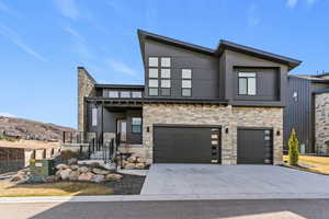 Contemporary house featuring stone siding, an attached garage, driveway, a mountain view, and a porch