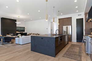 Kitchen with a spacious island, high end appliances, a large fireplace, light wood-style floors, and dark stone countertops