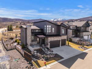 View of front of home with stone siding, an attached garage, a mountain view, concrete driveway, and covered porch