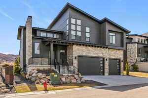 Contemporary home featuring stone siding, a garage, driveway, and a chimney