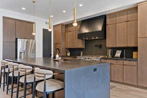 Kitchen featuring a breakfast bar area, a large island with sink, extractor fan, stainless steel appliances, and light wood finished floors