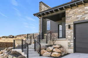 Entrance to property featuring stone siding, a garage, and a chimney