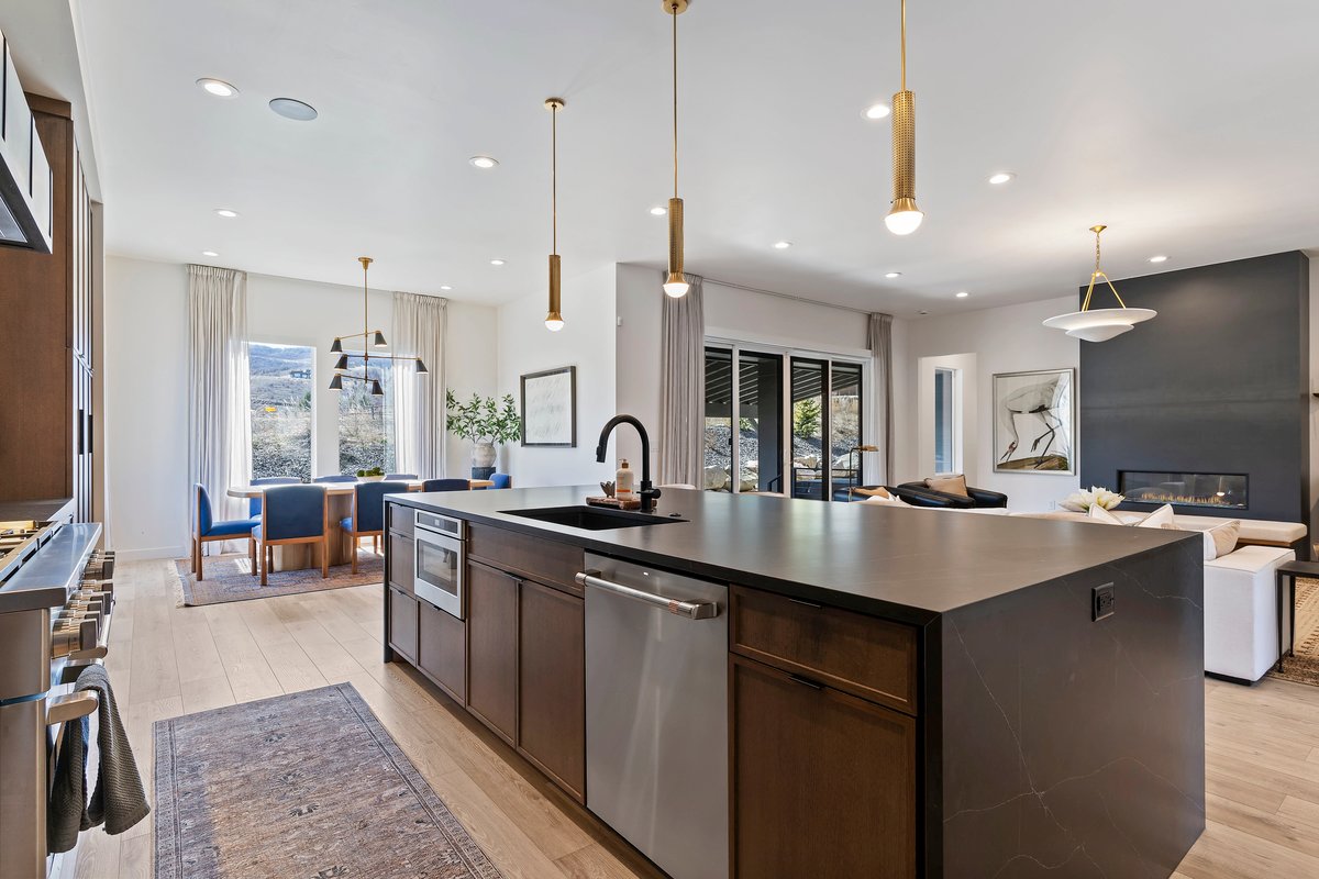 Kitchen with an island with sink, light wood-style floors, stainless steel appliances, dark wood finish cabinetry, and hanging light fixtures