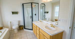 Bathroom with double vanity, a bath, a shower stall, light tile patterned floors, and suspended lighting