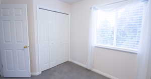 Unfurnished bedroom featuring dark carpet, a closet, and multiple windows