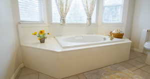 Primary full bath featuring light tile patterned flooring, a bath, and healthy amount of natural light