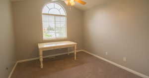 Office area with ceiling fan, dark colored carpet, and vaulted ceiling