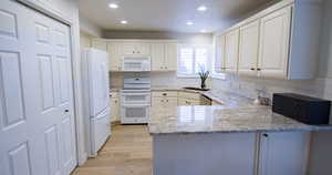 Kitchen with a peninsula, white appliances, light stone countertops, light wood-style floors, and recessed lighting