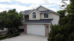 Traditional-style home featuring concrete driveway, a shingled roof, an attached garage, and brick siding