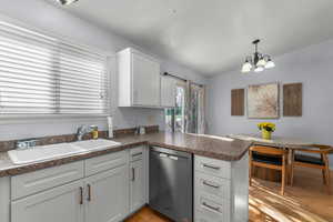 Kitchen featuring a peninsula, stainless steel dishwasher, dark countertops, white cabinets, and light wood finished floors