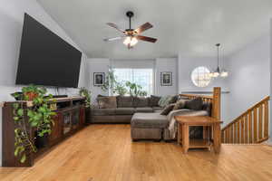Living room featuring light wood finished floors, suspended lighting, ceiling fan, and lofted ceiling