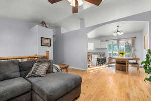 Living room featuring arched walkways, a ceiling fan, light wood-style flooring, hanging lights, and vaulted ceiling