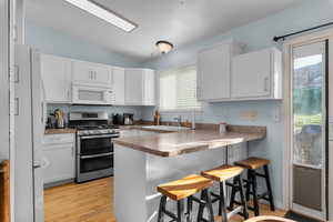 Kitchen with a breakfast bar area, a peninsula, white appliances, white cabinets, and light wood-style flooring