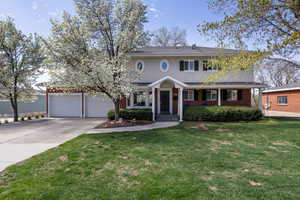 View of front of property featuring a front lawn, driveway, brick siding, covered porch, and an attached garage