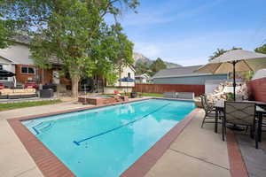 View of swimming pool with patio surround, an outdoor living / dining area, an in-ground hot tub, a fenced backyard, and a mountain view