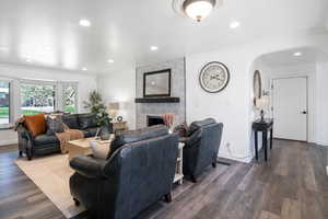 Living room with arched walkways, dark wood-style floors, crown molding, a large fireplace, and recessed lighting