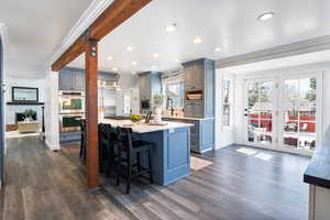 Kitchen featuring built in appliances, a breakfast bar, a center island with sink, crown molding, and dark wood-style flooring