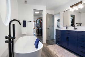 Full bath with a walk in closet, vanity, a freestanding bath, and dark wood-type flooring