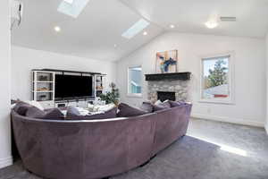 Carpeted living area with a stone fireplace, recessed lighting, a high ceiling, and a skylight