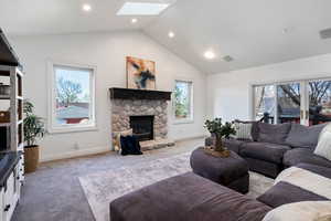 Living area featuring carpet flooring, a skylight, healthy amount of natural light, a stone fireplace, and recessed lighting