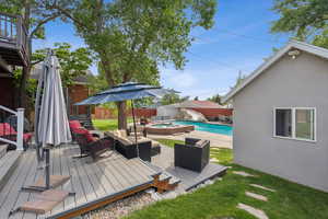 Wooden terrace with a patio, a fenced backyard, an outdoor living space, and a pool with connected hot tub