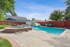 View of pool with outdoor dining space, patio surround, an in-ground hot tub, and a fenced backyard