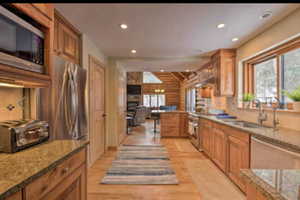Kitchen with stainless steel appliances, light stone counters, recessed lighting, rustic walls, and light wood finished floors