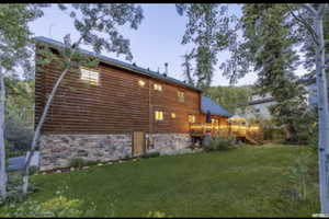 Back of property featuring a lawn, a wooden deck, and stone siding