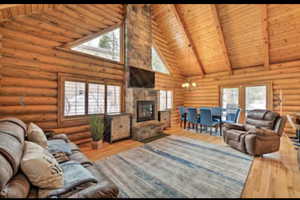 Living area with a high wooden beamed ceiling, wood finished floors, suspended lighting, log walls, and a fireplace