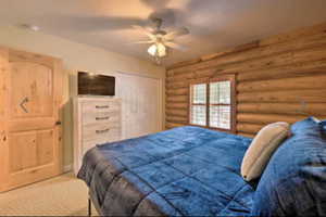 Carpeted bedroom with log walls, a closet, and a ceiling fan