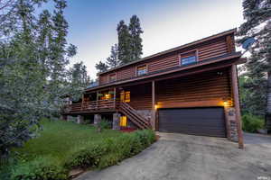 Cabin with a front lawn, an attached garage, driveway, stone siding, and log exterior