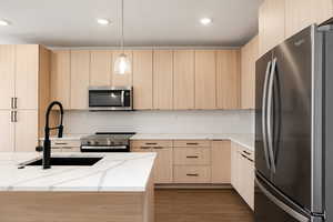 Kitchen featuring stainless steel appliances, light wood finish cabinetry, light stone counters, modern cabinets, and decorative backsplash